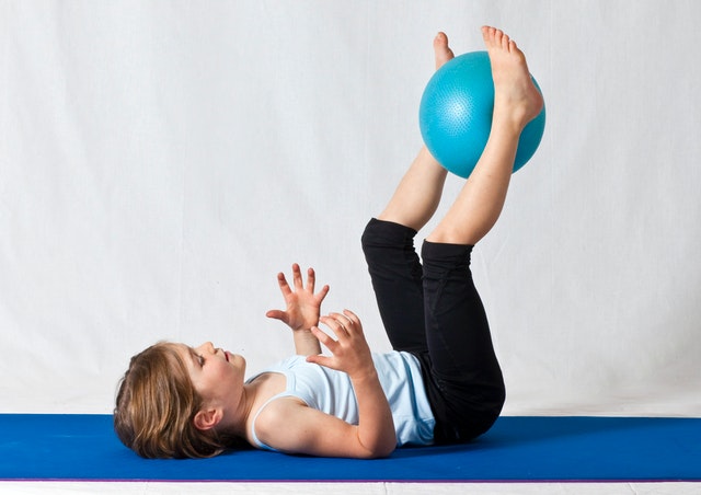 A kid is playing with a blue exercise ball.