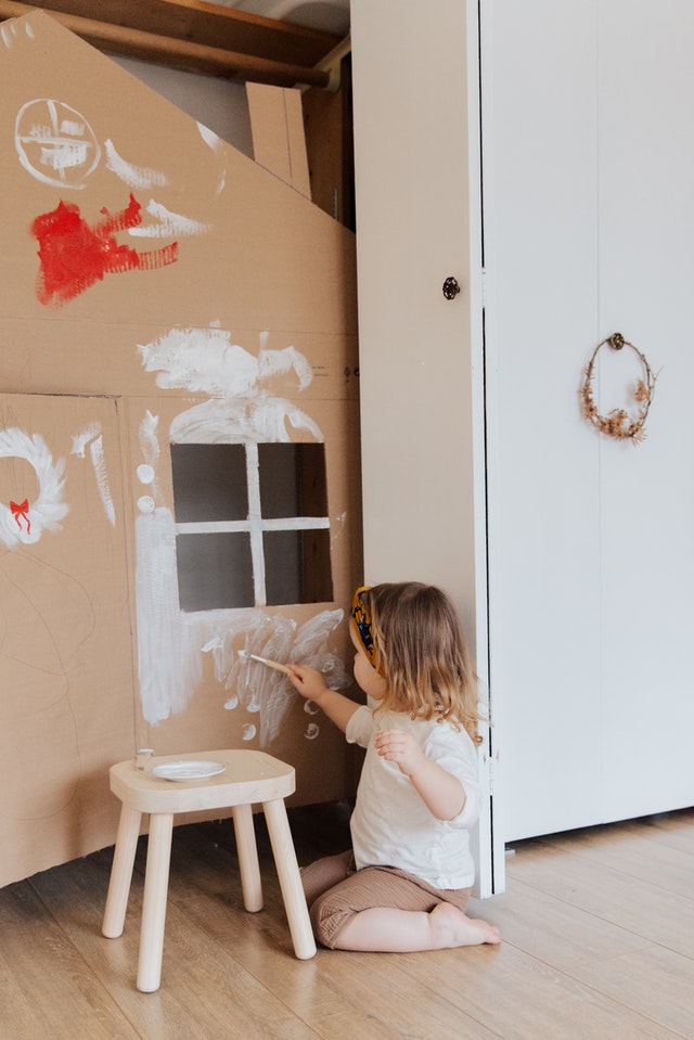 A kid is painting a home made out of card box.